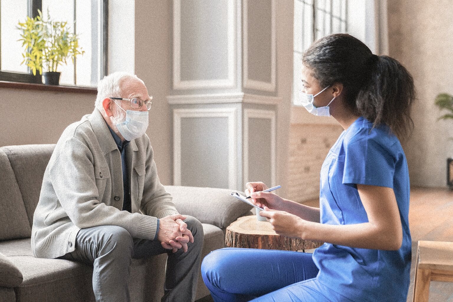 A case manager works with an elderly client while both are seated and wearing masks..