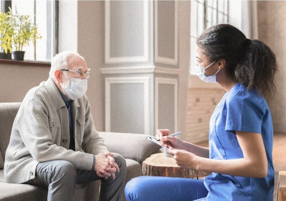 A case manager works with an elderly client while both are seated and wearing masks.