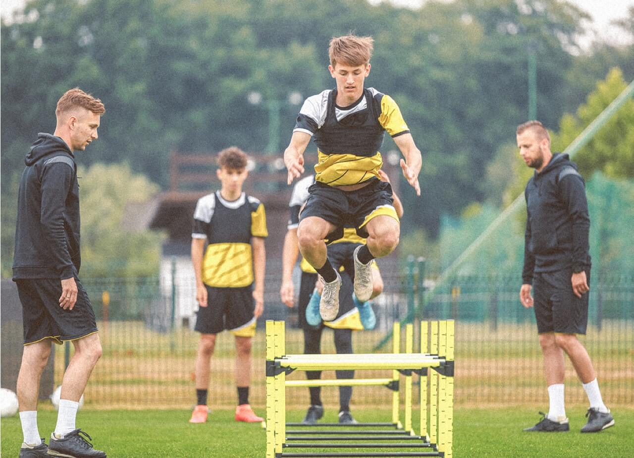 Student athletes jump over hurdles on a field.