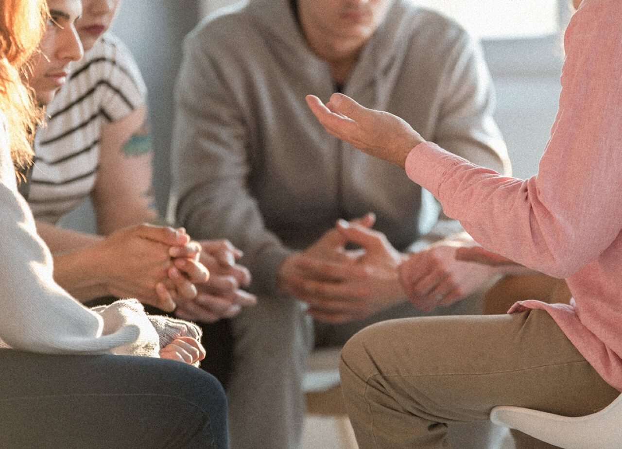 A drug and alcohol counselor sits with a group to discuss issues and treatment. Closeup without faces.
