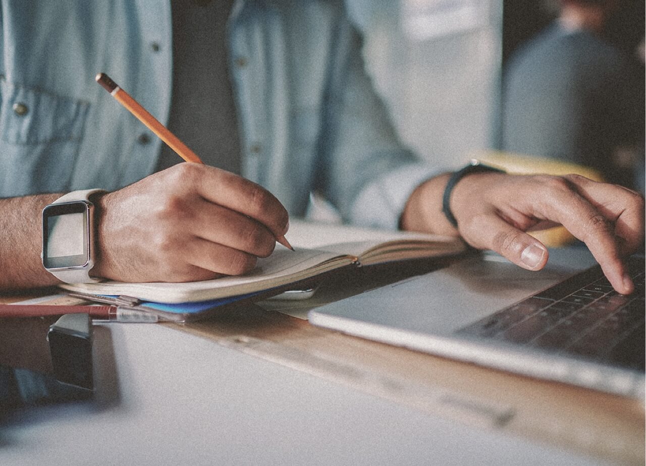 A person studying on a computer and taking notes in a note book. Closeup of hands.