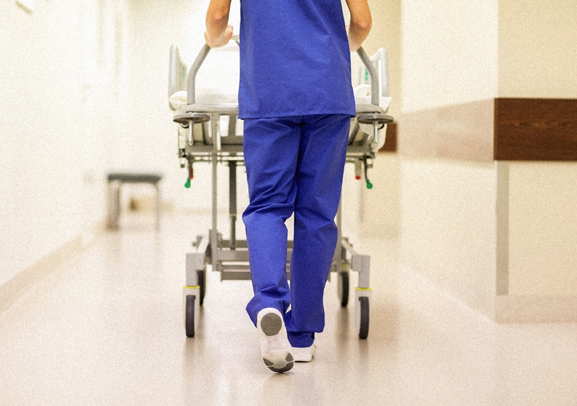 A CRNA walking down a hospital hall while wheeling a patient on a stretcher.