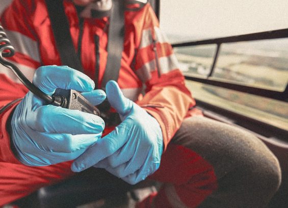 A flight nurse holds a walkie talking while riding in a helicopter wearing blue gloves. Close-up.