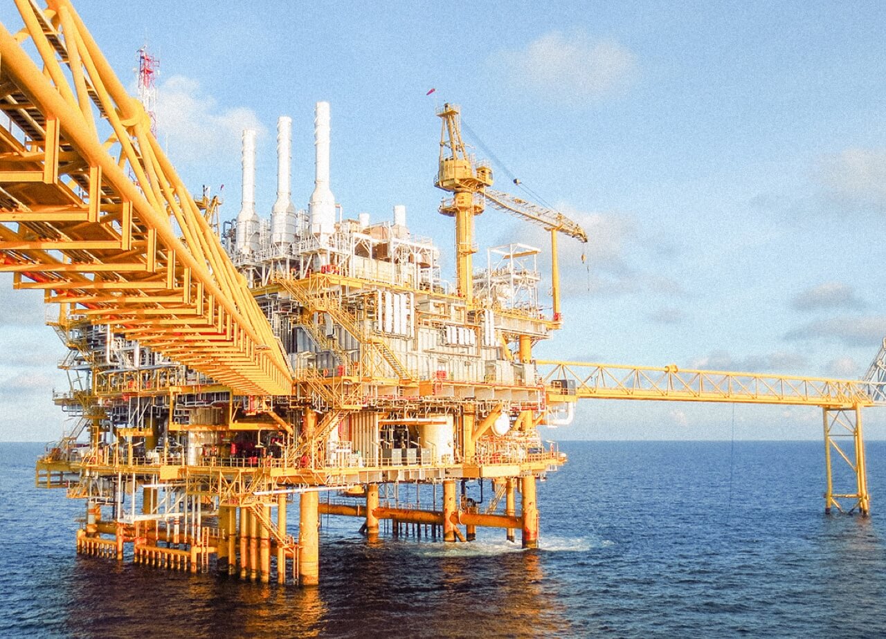 An orange oil rig in the ocean shown on a sunny day.