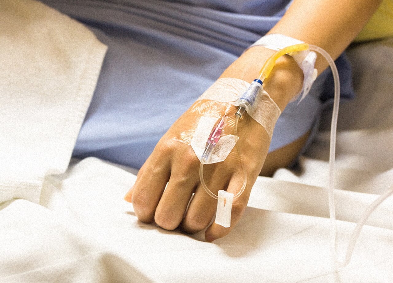 A person with an IV line going into their left hand. Close-up.