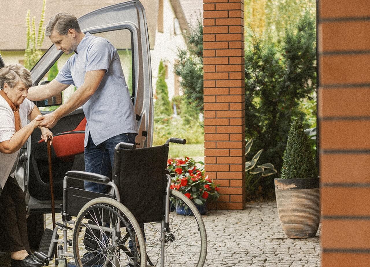 A caregiver helps a patient out of a car and into a wheelchair.