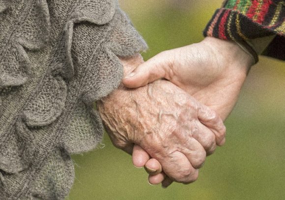 An elderly person holding hands with another person. Close up.