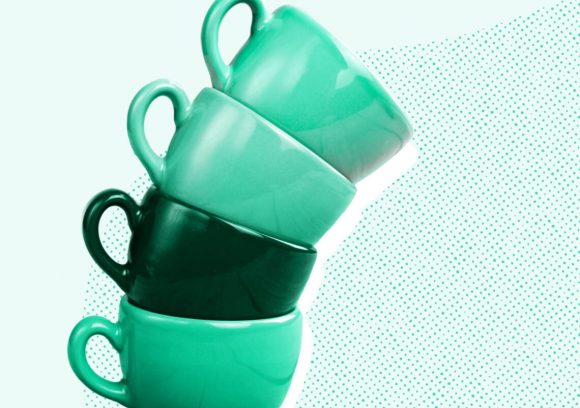 Four green coffee mugs stacked precariously about to tip over on a light green background.