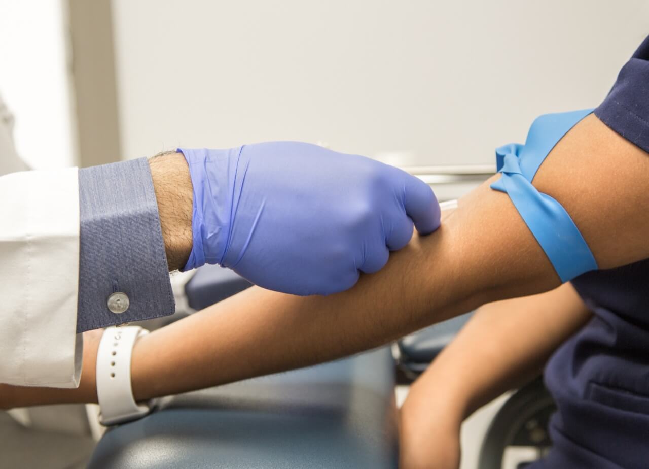 A phlebotomist draws blood from a patient's arm.
