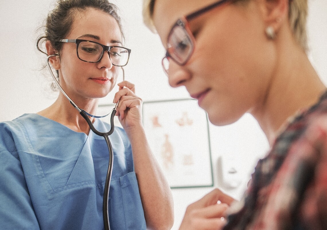 A Gerontology Nurse Practitioner checks the heartbeat of a patient with a stethoscope.