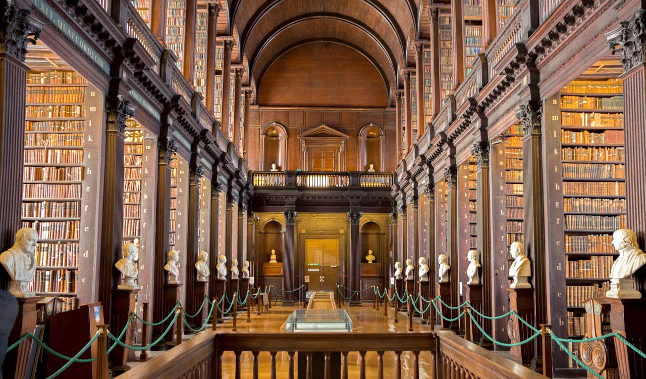 A large prestigious library with many books, arches, and white marble busts.