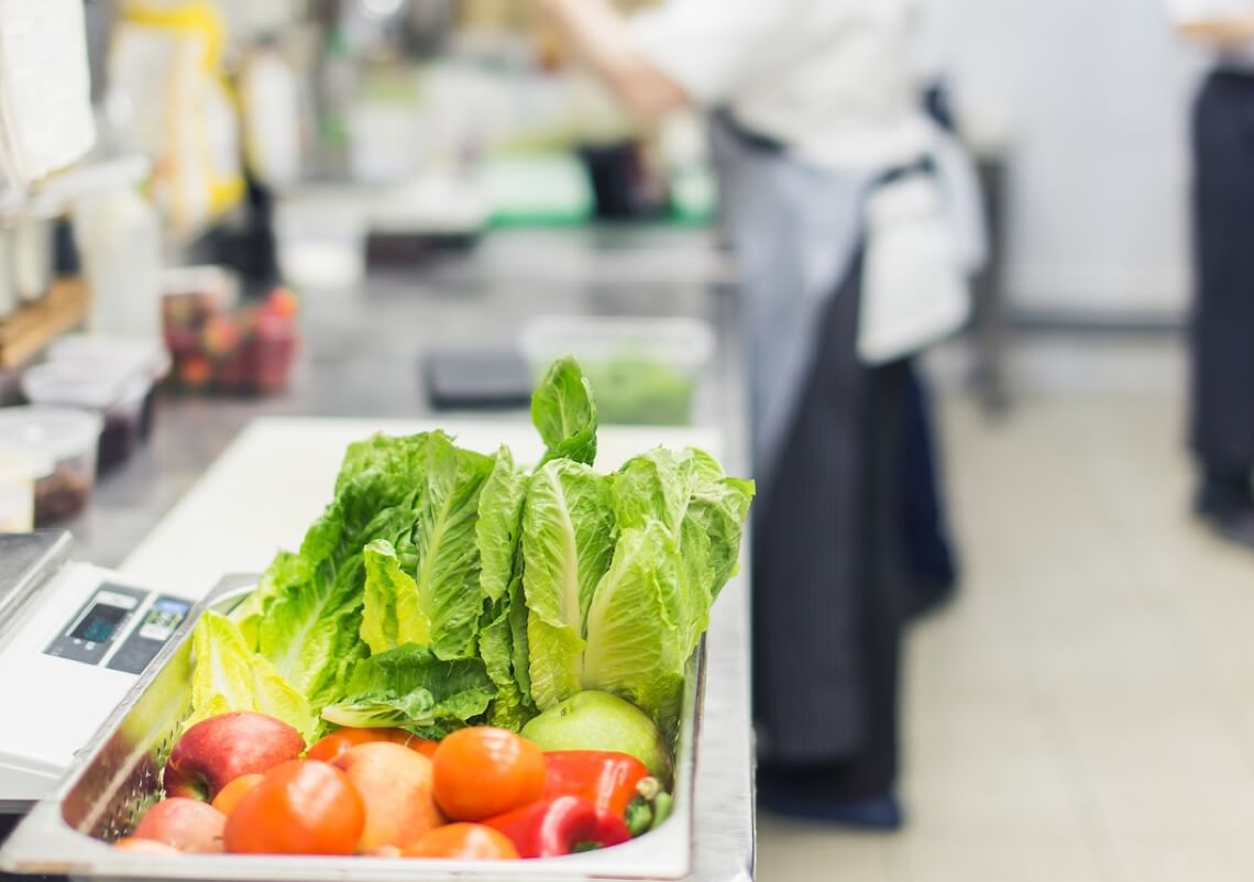 Lettuce and tomatoes in a prep bowl on a counter in a restaurant kitchen.