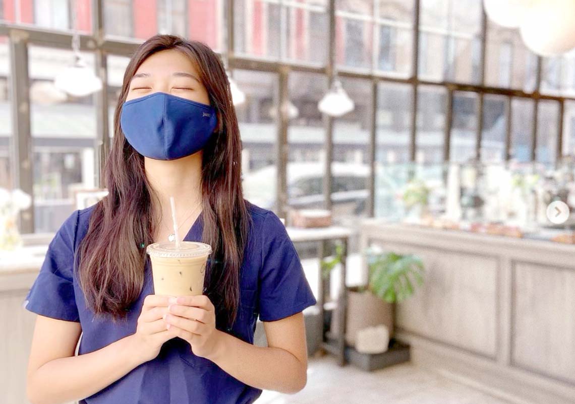 Phyician assistant wearing a mask while holding an iced latte.