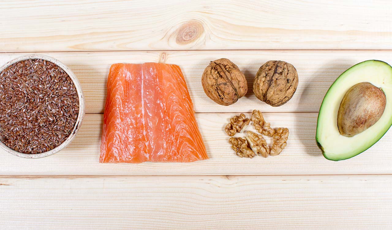 Flax seeds, salmon, walnuts and avocado lined up on a wood table.