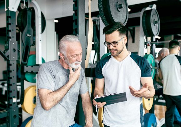 A male personal trainer workin in a gym with an older mail client looking at a workout plan.