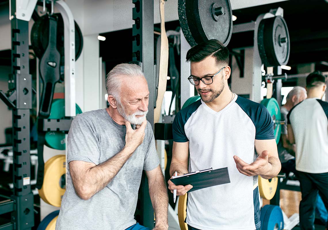 A male personal trainer workin in a gym with an older mail client looking at a workout plan.