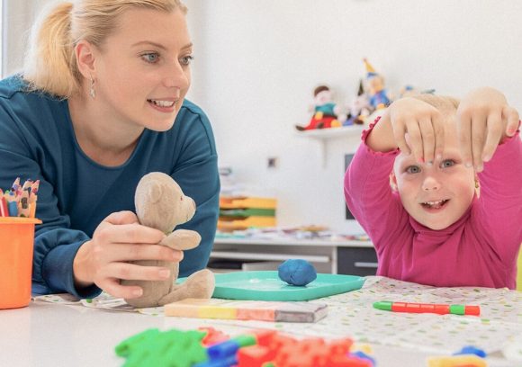 A young female occupational therapist working with a small child at a table with toys.