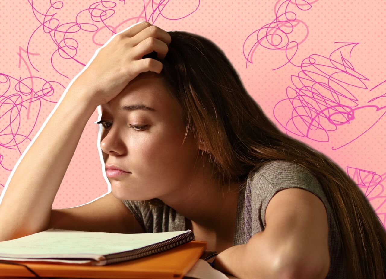 A young woman with straight brown hair looks tired and stressed while leaning on a table with books and papers. Pink background.
