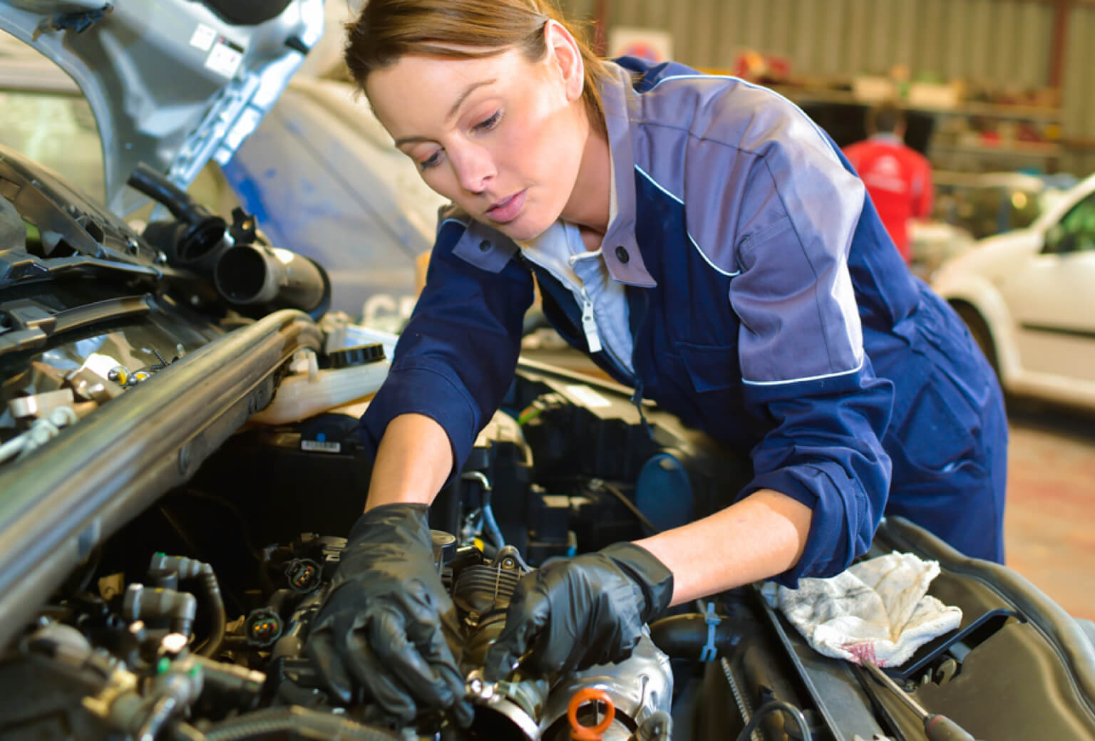 A young, white female auto mechanic works under the hood of a car on the engine.