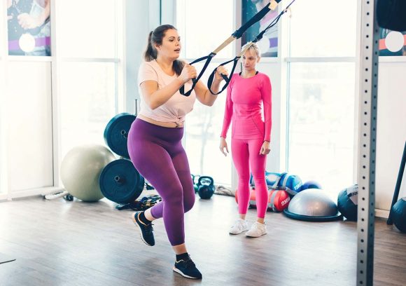 A female personal trainer wearing all pink works with a client using a TRX strap.