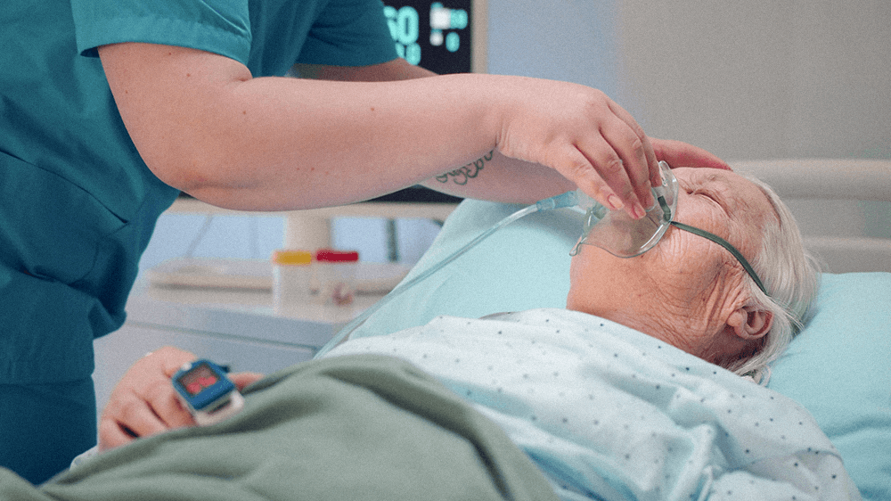 A stroke-certified nurse places an oxygen mask on an elderly patient in a hospital bed.