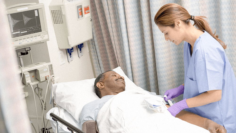 An ambulatory perianesthesia nurse checks on a recovering patient in a hospital bed during post-op.