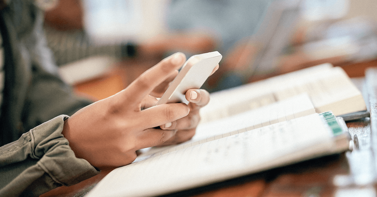 Close-up of a person holding a smartphone over an open notebook on a desk.