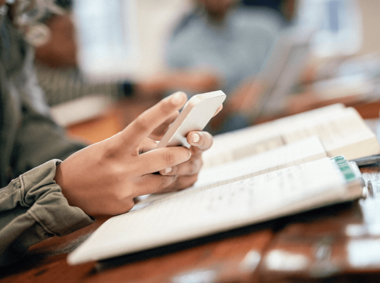 Close-up of a person holding a smartphone over an open notebook on a desk.